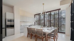 Een moderne keuken met witte kasten, een ingebouwde magnetron en een eethoek met rieten stoelen en een witte tafel.