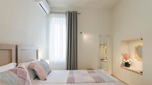 A bedroom with two beds, a large window with curtains, a mirror, and a small shelf with a vase. - Leny's Seafront House (Panormos)