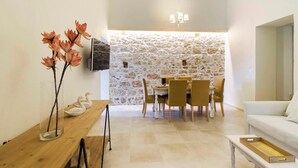 A dining area with a stone wall, a wooden table, and a white sofa. - Leny's Seafront House (Panormos)