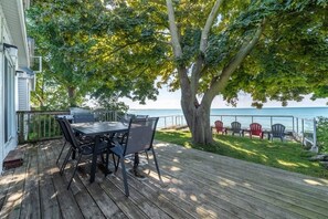 A wooden deck with a table and chairs, overlooking a body of water. - Prince Edward County Lakehouse 3 Bedroom and 3 Bathroom (Prince Edward)