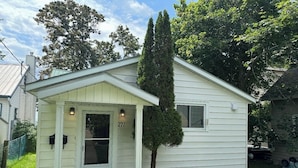 A small, single-story house with a white exterior, a front door, and a small porch.
