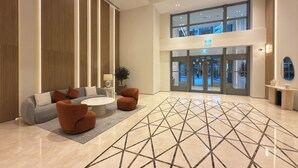 Un hall d’entrée spacieux au design moderne, comprenant un espace détente avec des canapés et des fauteuils, une table basse centrale et un sol orné de motifs géométriques.