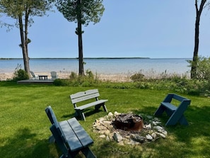 Un espace extérieur aménagé au bord du lac, avec un foyer, des bancs et des fauteuils Adirondack.