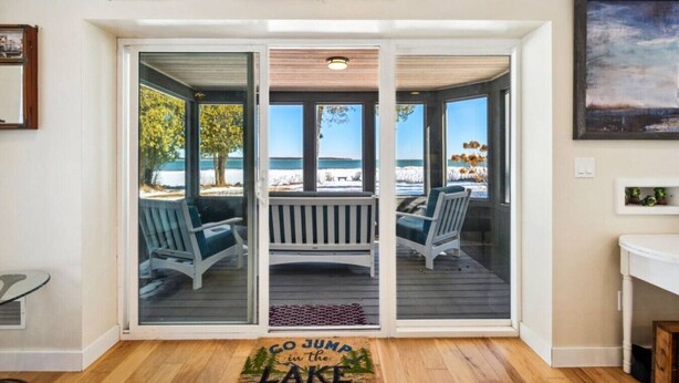 A room with a sliding glass door leading to a deck with two chairs and a view of the beach.