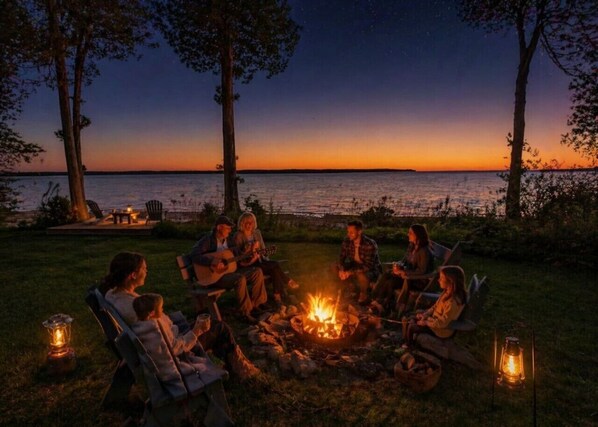 A group of people around a campfire at dusk with a view of the water.