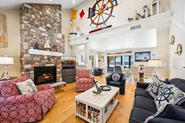A spacious living room with a stone fireplace, nautical decor, and a view of the sea.