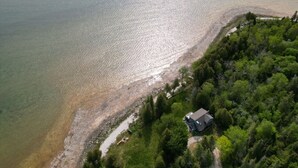 An aerial view of a coastal property with a house near the water, surrounded by dense greenery.