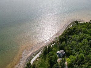 An aerial view of a coastal property with a house near the water, surrounded by dense greenery.
