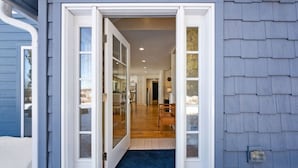 A house entrance with a blue exterior, a wooden floor, and a blue carpet leading inside.