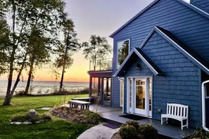 Uma casa à beira-mar com varanda coberta, um banco e vista para o oceano.