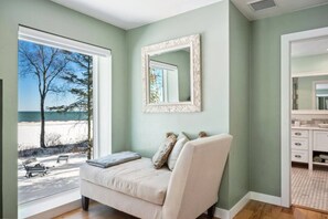 A bedroom with a large window, a bed, a mirror, and a view of the beach.