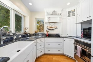 Une cuisine moderne avec des meubles blancs, des plans de travail en granit, un four encastré et une fenêtre donnant sur un espace verdoyant.