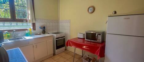 A compact kitchen with basic appliances, a sink, and a window with a view of greenery.