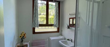 Un baño pequeño con ventana, lavabo, lavadora y ducha.