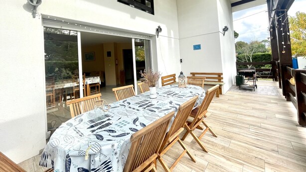 A covered patio with a dining table and chairs, a sliding glass door leading to an interior space, and a sign indicating a play area. - Villa Colombe by Agence Bru - 453196 (Carcans)