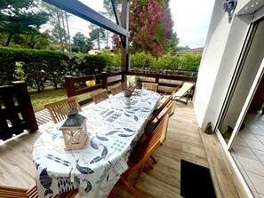 Un patio al aire libre con una mesa y sillas de madera, un farol y vistas del jardín y los árboles circundantes.