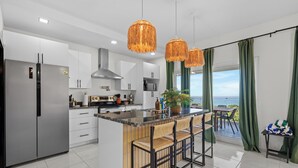 A modern kitchen with a central island, stainless steel appliances, and a view to the outside. - Endless Island Horizons @ Coral Views, French Harbor (French Harbor)