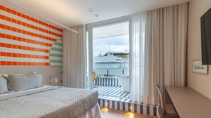Ein modernes Hotelzimmer mit einem großen Bett, Blick auf die Stadtlandschaft, einem Balkon mit Streifenböden und einem Essbereich.