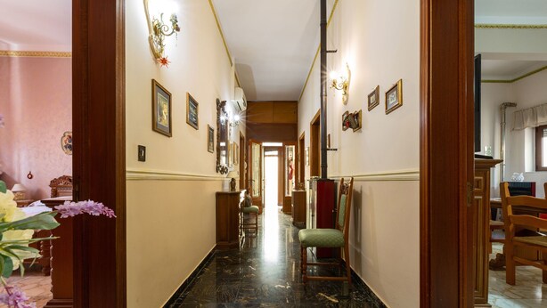 A hallway with a marble floor, wooden doors, and framed pictures on the walls.