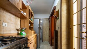 A narrow kitchen with wooden cabinets, a gas stove, a refrigerator, and a window with a view.