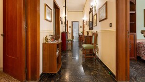 A hallway with wooden doors, a marble floor, and framed artwork on the walls.