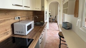 A modern kitchen with white cabinets, a wooden countertop, a microwave, a toaster, and a dining area with a chair and table. - Apartment with large terrace, close to beaches, center and tourist sites! (Hyères)