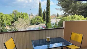 Un balcón con dos sillas amarillas y una mesa de vidrio, con vista a un estacionamiento y vegetación.