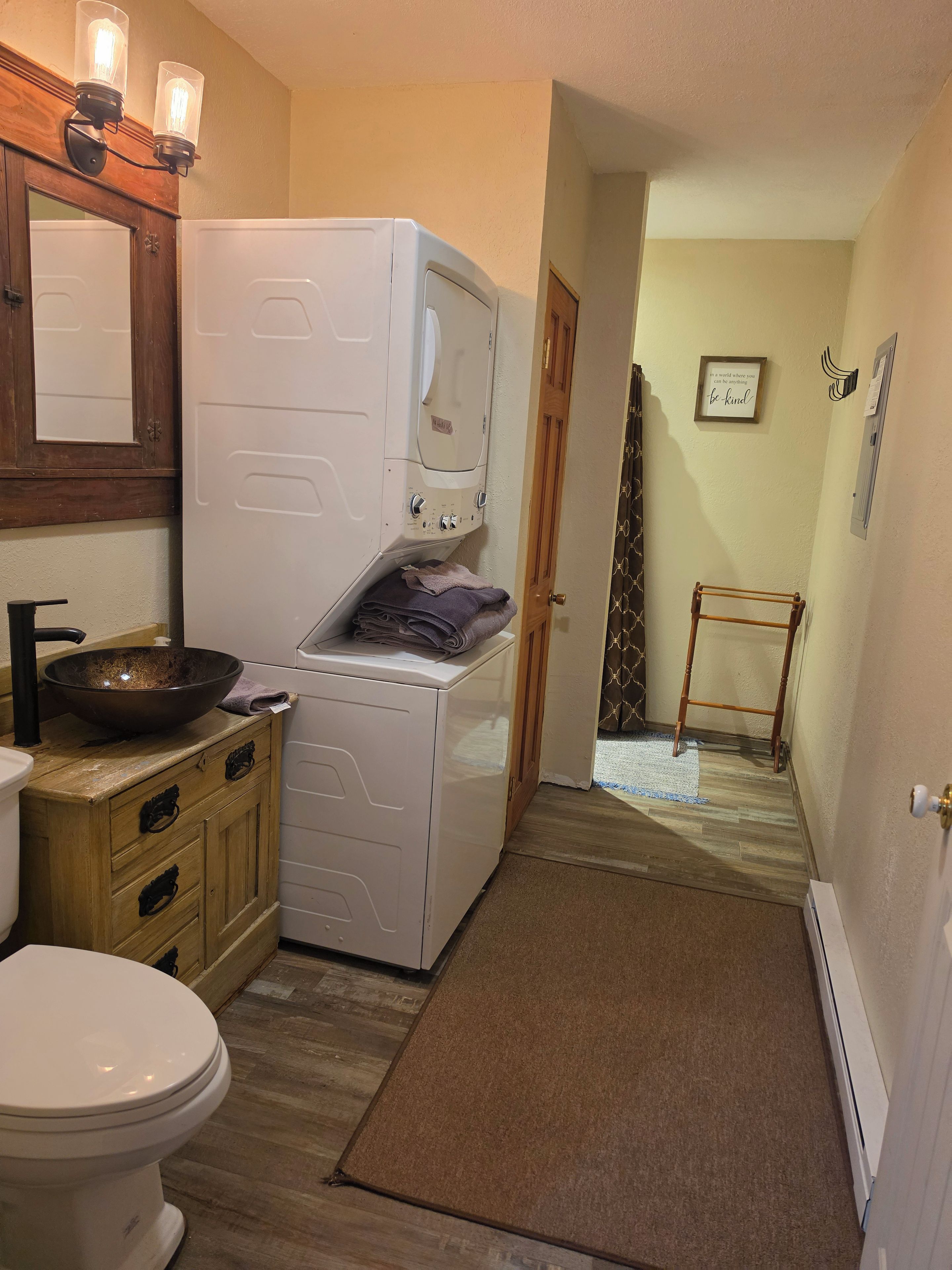 A compact bathroom with a white toilet, a washing machine, and a wooden cabinet.
