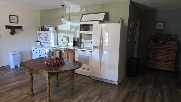 A kitchen with a wooden dining table, white appliances, and a decorative sign. - Hayfield Cabin (Niota)