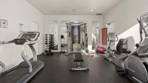 Ein Fitnessstudio mit Laufbändern, Crosstrainern, einer Gewichtbank und Kurzhanteln.