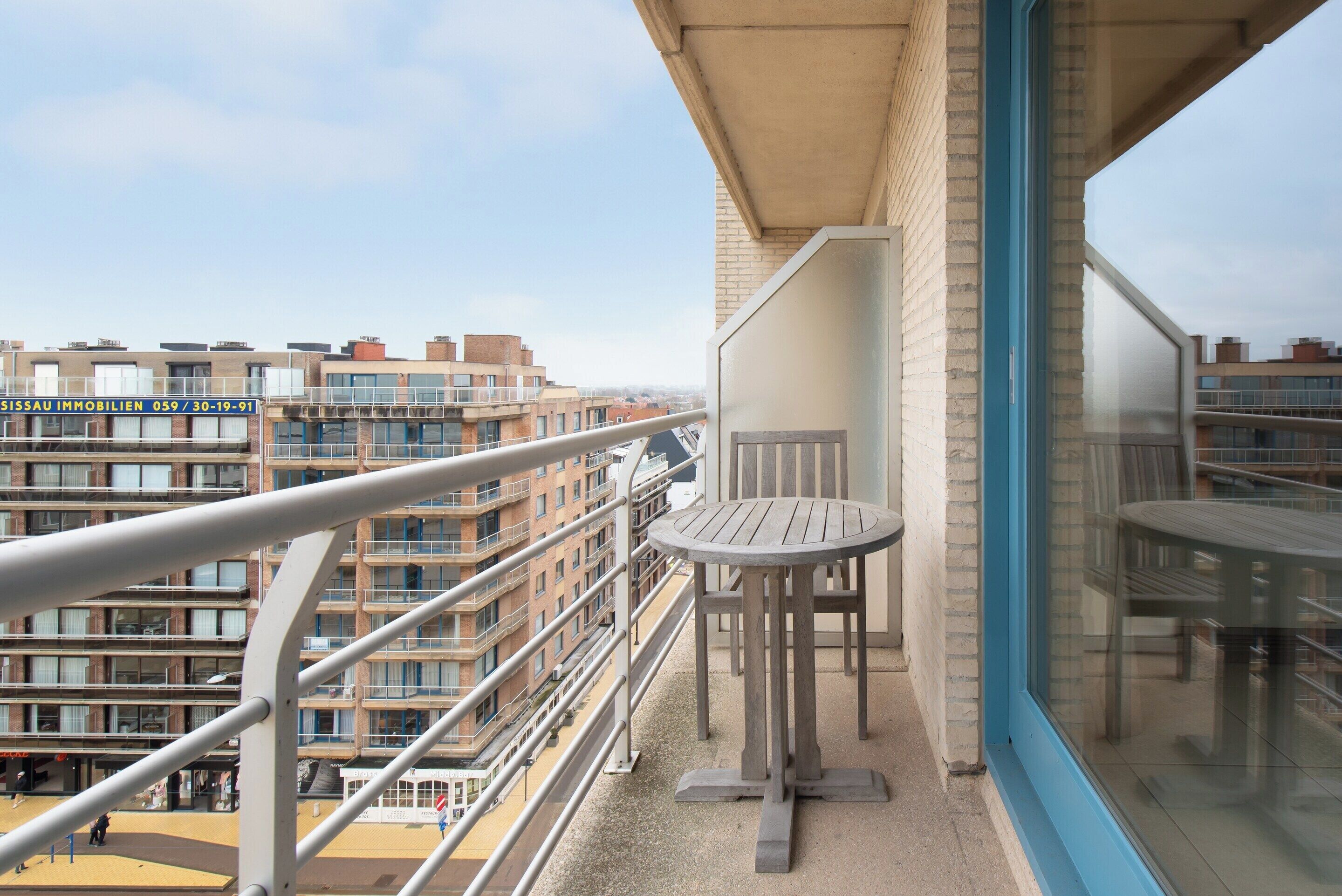 A balcony with a table and chairs, overlooking a residential area with multiple apartment buildings.