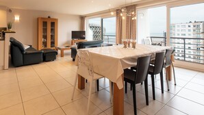 Un salon moderne comprenant un coin repas, un canapé, un téléviseur et une grande fenêtre offrant une vue sur la ville.