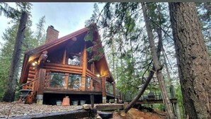 Un chalet rustique doté d’une terrasse en bois, entouré d’arbres et d’un paysage naturel.