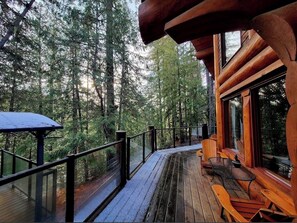 Une terrasse en bois avec une rambarde en verre donnant sur une zone boisée.