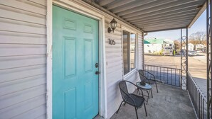 A turquoise door with the number 105, a covered porch with metal railings, and a view of a parking lot. - Cozy 2 Bedroom Getaway (Covington)