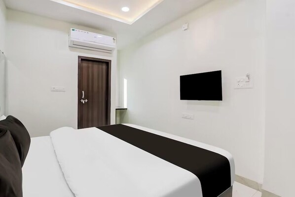 A hotel room with a bed, a flat-screen TV mounted on the wall, an air conditioning unit above the door, and a window with curtains. - Wishotel Inn (Indore)