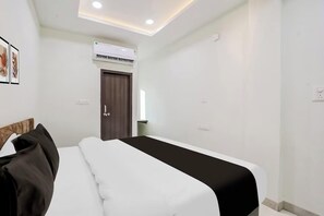 A hotel room with a bed, a wardrobe, an air conditioning unit, and a door. - Wishotel Inn (Indore)