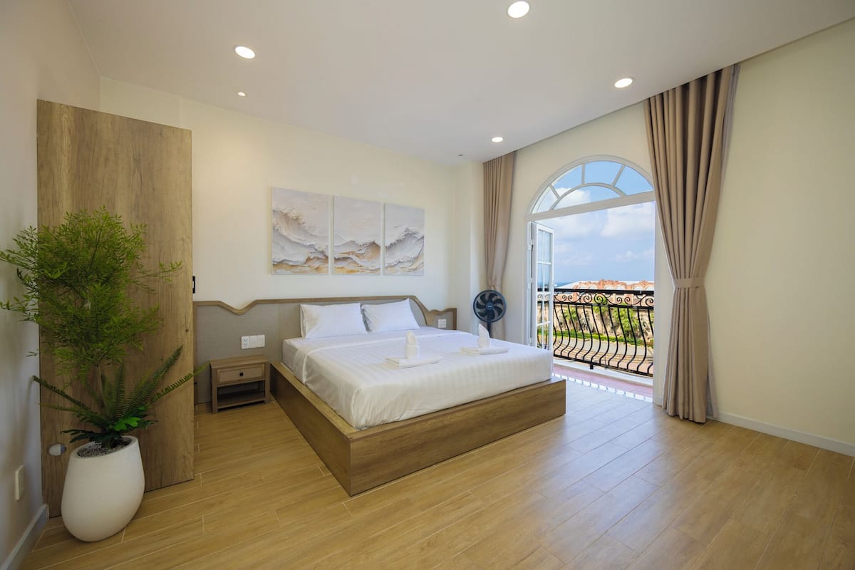 A modern bedroom with a large bed, a potted plant, and a balcony with a view.