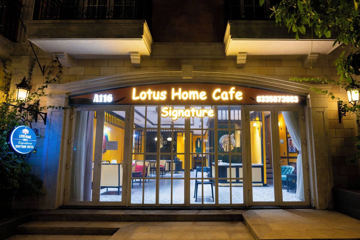 The exterior of Lotus Home Cafe with a glass door entrance, a neon sign, and a visible interior through the glass.