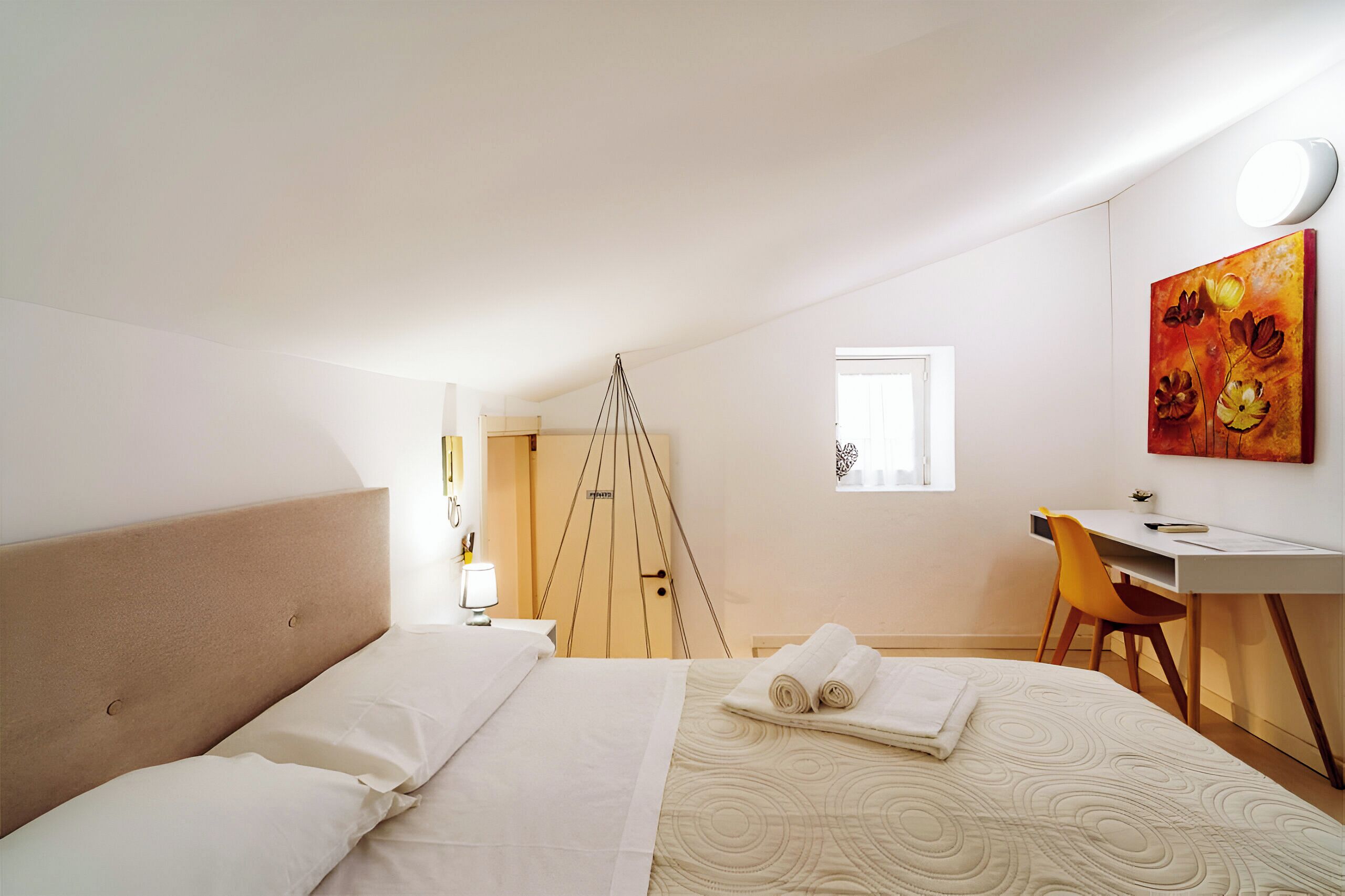 A hotel room with a bed, a desk, a chair, a painting, and a window.
