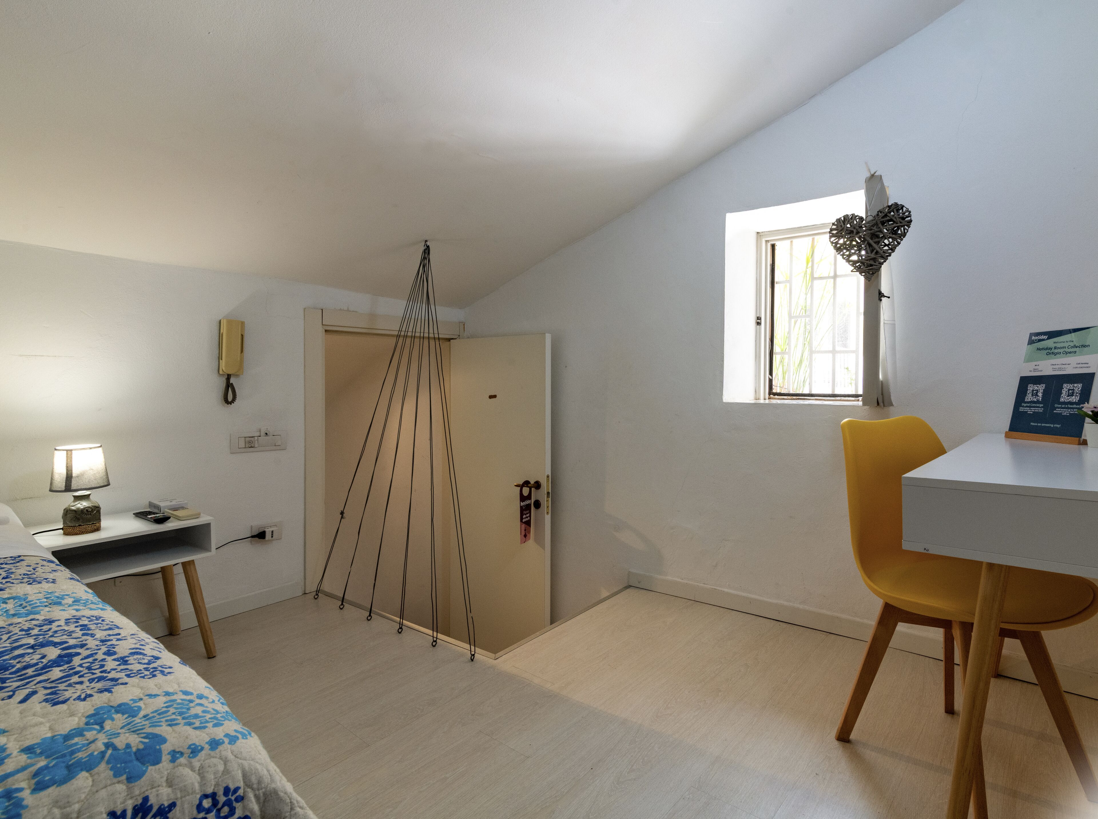 A room with a bed, a desk, a chair, a hanging light fixture, and a window.
