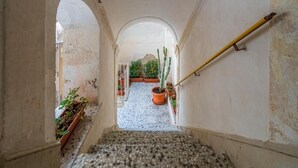 Un corridoio stretto con pavimento piastrellato, porte ad arco e piante in vaso.