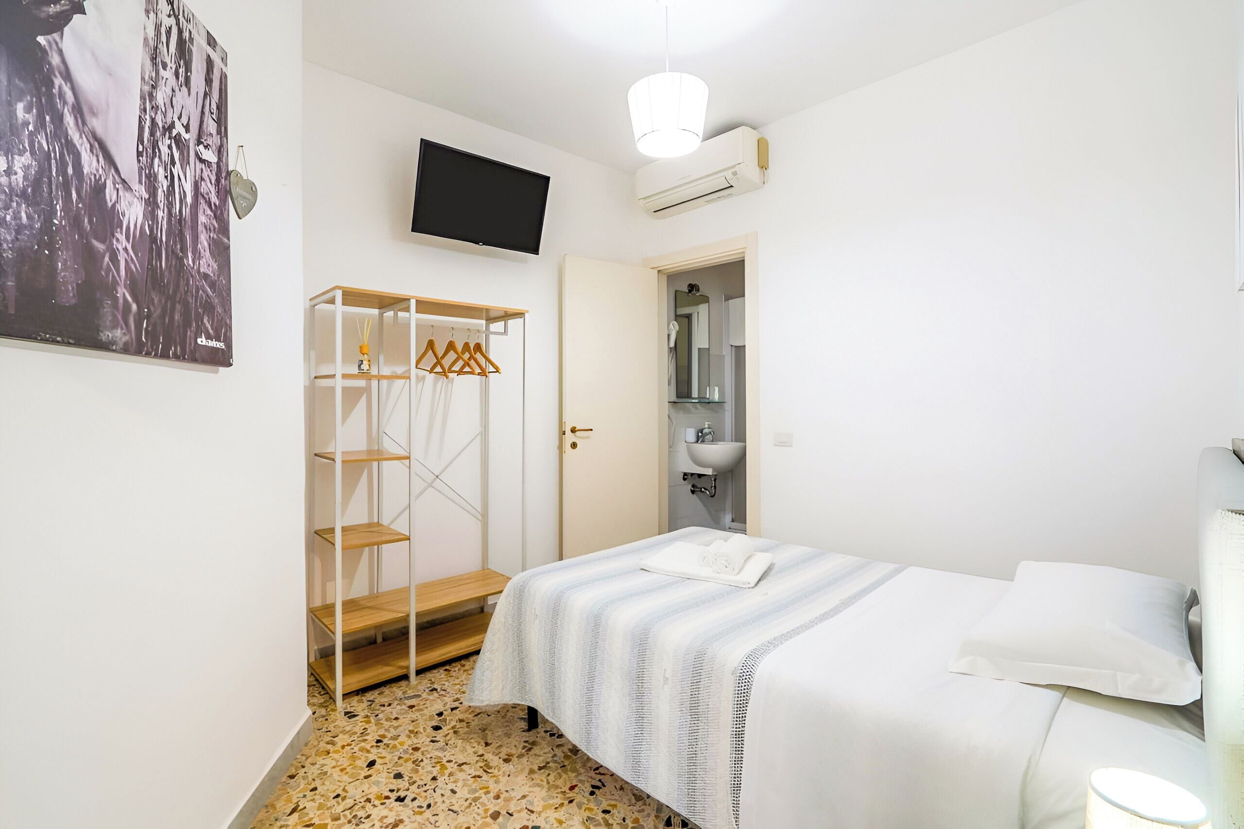 Een slaapkamer met een bed, een kledingkast, een televisie en een zichtbare badkamer door een geopende deur.
