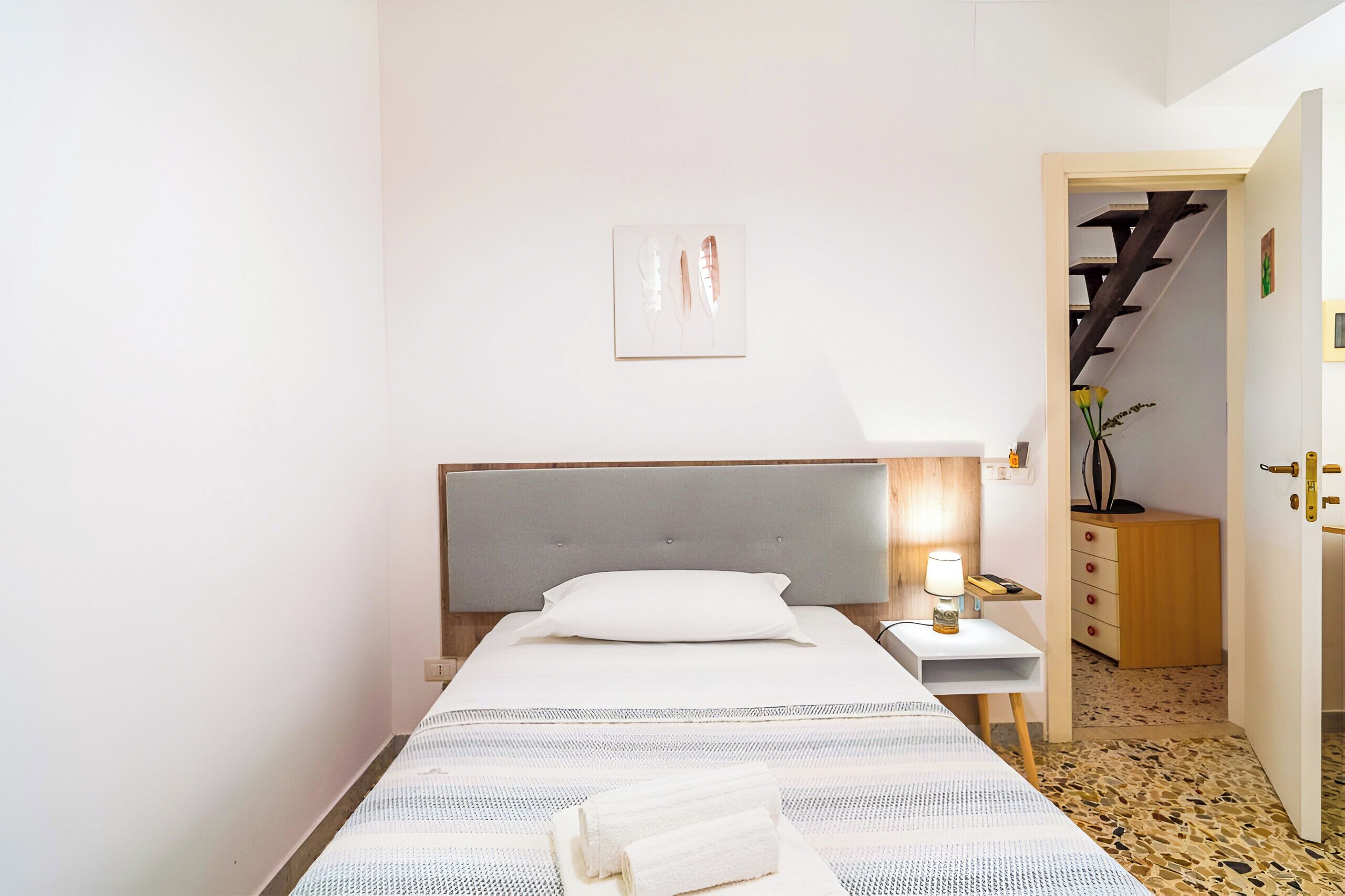 A small, neatly arranged bedroom with a bed, bedside table, and a lamp.