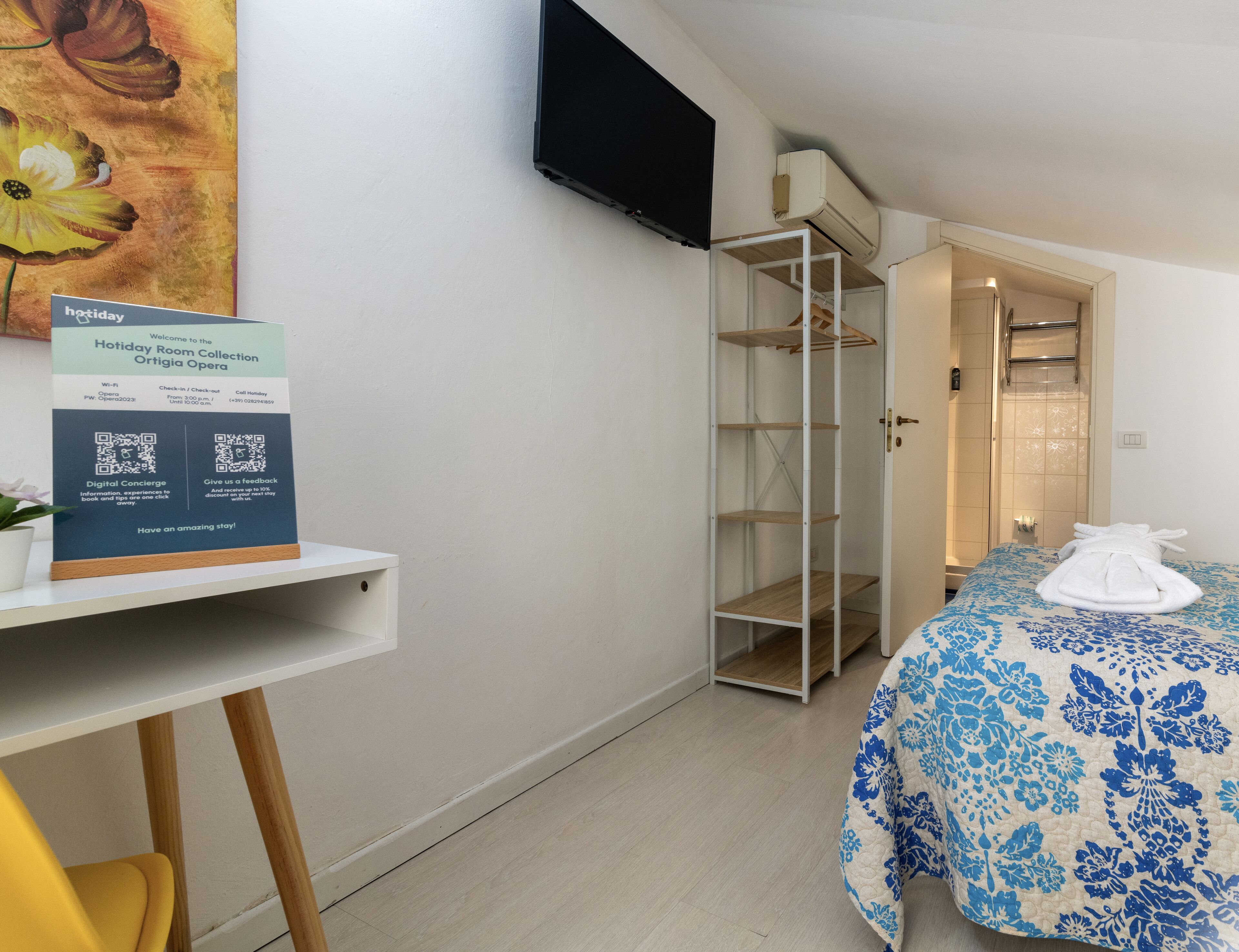 Ein Hotelzimmer mit Bett, Schrank, an der Wand montiertem Fernseher und einem Schild mit QR-Codes.