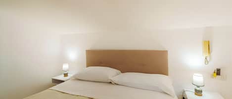 A neatly made bed with a headboard, two bedside tables with lamps, and a wall-mounted phone.