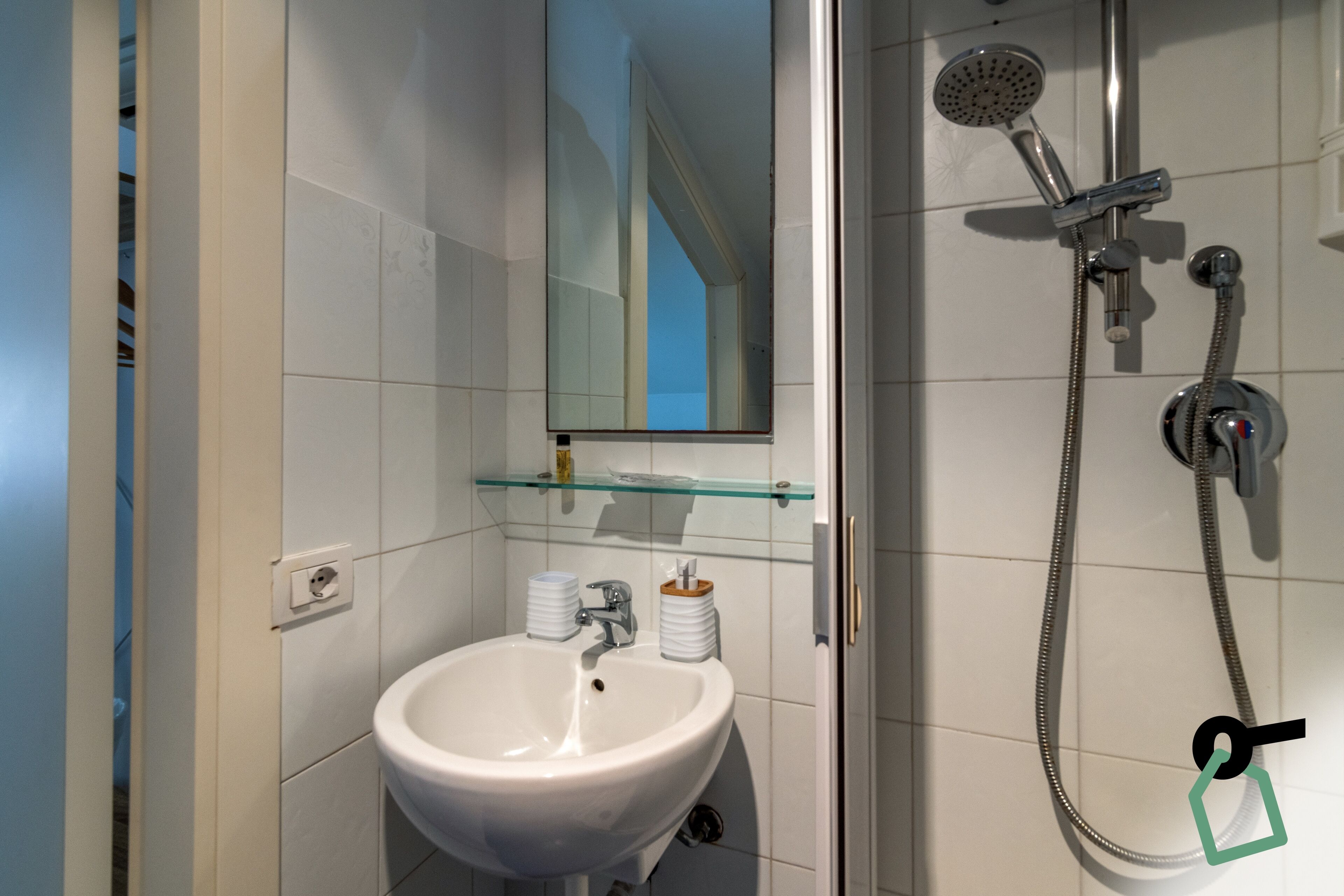 A bathroom with a white sink, a glass shelf, and a shower with a handheld showerhead.