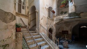 Un edificio storico con una scalinata centrale, portali ad arco e un cortile con piante in vaso e biciclette.