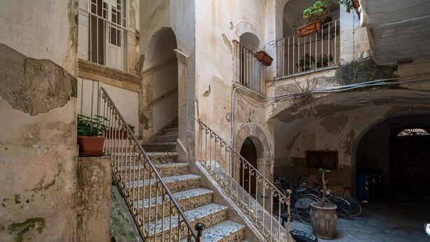 Un bâtiment historique doté d’un escalier central, de portes en arc de cercle et d’une cour intérieure agrémentée de plantes en pot et de vélos.
