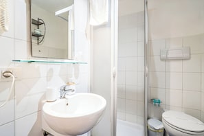 Een moderne badkamer met een douchecabine van glas, een witte wastafel met spiegel en een toilet.